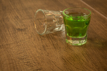 shot glasses lined up on wooden bar background filled with green spirit cocktail and shamrock,...