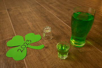 full pint and shot glass on wooden bar background filled with green spirit beer and shamrock, drunk...