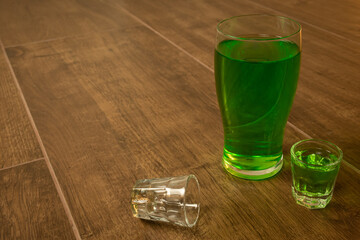 full pint and shot glass on wooden bar background filled with green spirit beer and shamrock, drunk...
