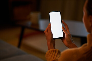 Young woman holding smartphone with white screen at home relaxing in dark