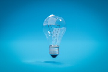 single glass lightbulb with filament wire floating in the air over infinite blue background; 3D Illustration