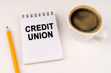 On a white surface, a cup of coffee, a pencil and a notepad with the inscription - CREDIT UNION