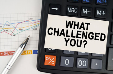 On the business chart lies a pen, a calculator and a business card with the inscription - What Challenged You