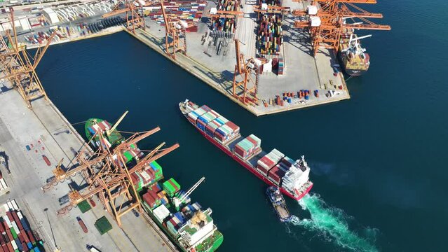 Aerial top down video of industrial cargo container ship being towed to logistics container terminal port to dock