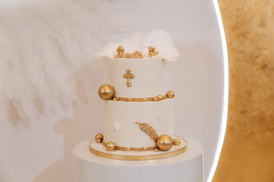 White luxury cake with gold decoration for baptism or birthday. Gold cross, balls and angel wings as decoration. Children's birthday celebration