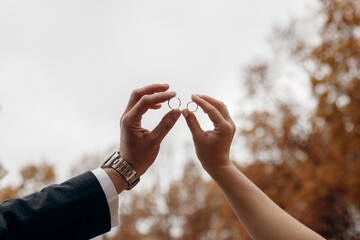 Male and female hands as silhouettes hold wedding rings facing each other. The bride and groom put...