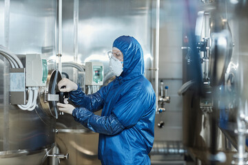 Man wearing protective gear and mask operating equipment at chemical factory