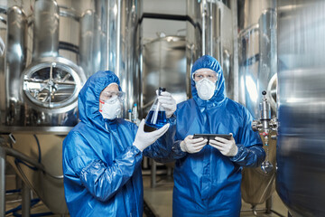 Two workers doing tests at chemical factory and wearing protective suits