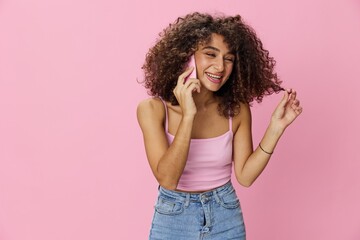 Woman with curly afro hair talking on phone in pink top and jeans on pink background, smile, happiness, copy space