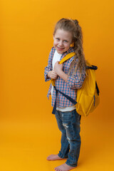back to school, cute joyful girl child 6-7 years old smiling on an isolated yellow background in with a school backpack. High quality photo