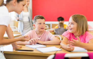 Fototapeta premium Preteen schoolchilds working in groups at lesson in primary school with teacher on background