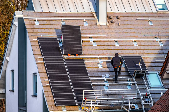 Construction workers install photovoltaic solar electric panels on the roof of a residential building