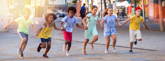 Obraz premium Group of smiling kids holding each other hands while running through city streets together.