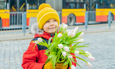 Beautiful boy on city street near bus stop with bouquet of tulips in his hands..