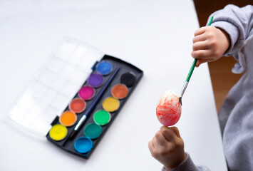 Close up of childrens hands holding easter egg and painting it with brush at home. Preparation for easter. Happy easter.