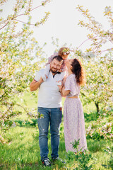Fototapeta premium a mom and a dad with a baby daughter in a blooming spring garden. happy family. 