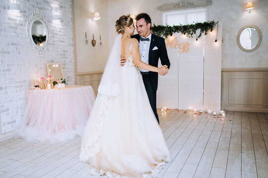 A young, stylish groom in a suit and a beautiful blonde bride with a diadem in a dress are hugging, dancing in a restaurant, indoors. Wedding portrait, photo of happy newlyweds.