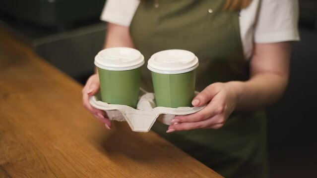 The barista's hands hold two green cups of ready-made latte. Close up