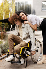 Pleasant, positive friends outdoors. A young man in a wheelchair, his girlfriend hugs him against the background of a building.