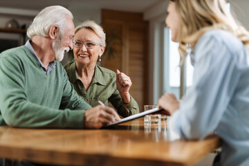 Happy senior couple signing a document with their financial advisor at home