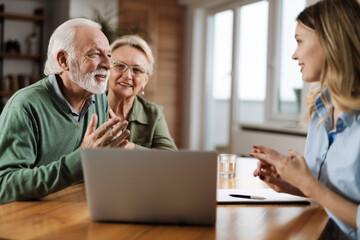 Happy mature couple and their counselor communicating while using laptop on a meeting at home