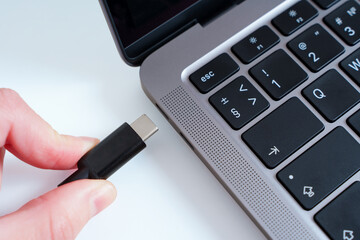 Close-up view of a hand plugging a USB Type-C cable into a laptop isolated. Modern ports...