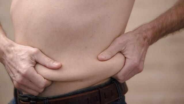 Man holds folds of fat on his stomach with his hands, turns to different sides. 