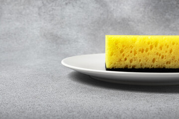 Yellow sponge for dishwashing on a white plate on a neutral gray background. Gentle dishwashing. House cleaning
