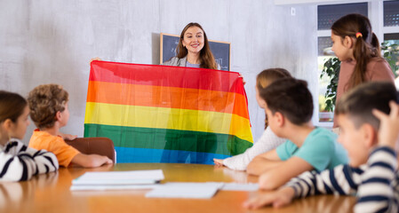 Kindly pedagogue demonstrating transgender flag to preteen pupils in teaching room during class