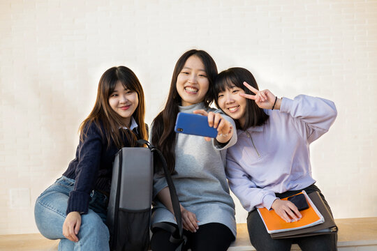 Group of Asian students on the street. The 3 women take a picture with the mobile in their class break time. Concept of education, friendship and social networks.