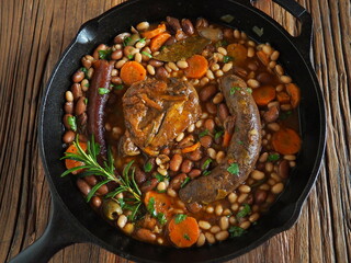 French Cassoulet, a meat and beans stew, in a cast iron skillet, on a rustic wooden table