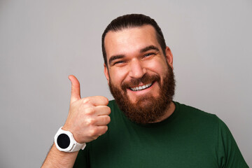 Naklejka premium Close up shot of a smiling man in green showing thumb up at the camera over grey background.