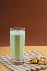 Plant-based natural pistachio milk on a beige background. Tall glass with pistachio milk on a linen napkin. Copy space