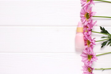 Cosmetic bottle on wooden table with pink daisy flowers