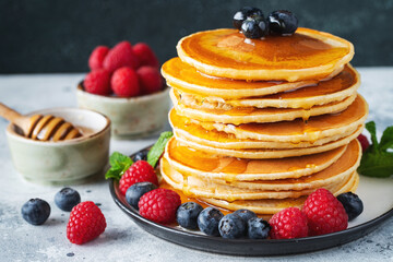 Delicious pancakes, with fresh blueberries, raspberry and maple syrup or honey on a dark background