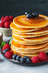 Delicious pancakes, with fresh blueberries, raspberry and maple syrup or honey on a dark background