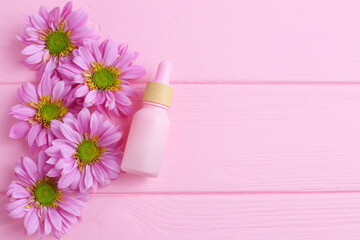 Cosmetic bottle on wooden table with pink daisy flowers