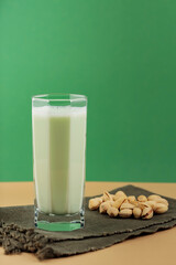Pistachio milk in the glass on a dark green linen napkin. Lactose free pistachio milk and scattered pistachios. Copy space