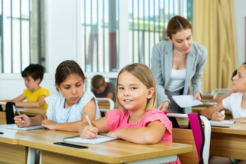 Portrait of two positive small school girls sitting together in classroom during lesson in elementary school