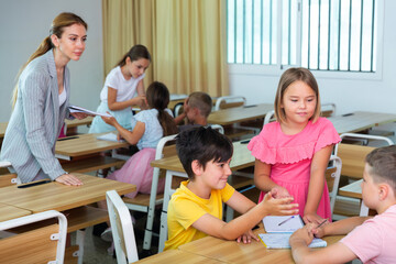 Fototapeta premium Schoolchildren performing group tasks in classroom. Teacher standing beside and observing.
