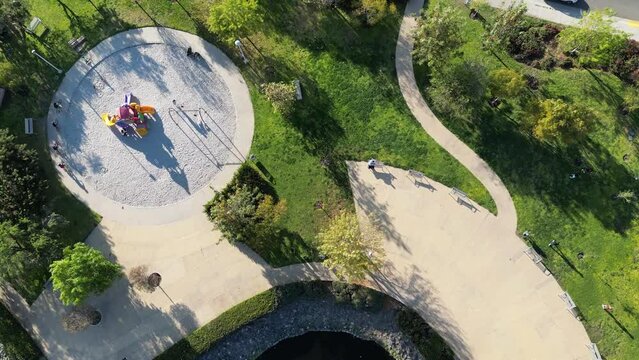 aerial view of a park with lake, fountain, playground with people on bicycles in a late afternoon day