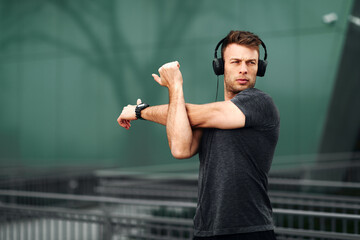 Young man stretching hands before jogging in sports clothes and headphones on his head