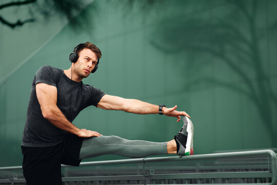 Young Man Stretching Hands Before Jogging In Sports Clothes And Headphones On His Head