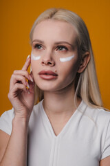 Beauty portrait image of pretty woman cosmetic cream treatment with anti aging isolated over yellow background, skin lifting and nourishing effect. Therapy