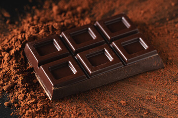 Dark and milk chocolate with nuts on a dark background sprinkled with cocoa powder.