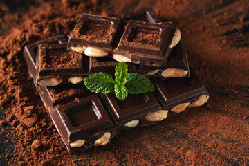 Dark and milk chocolate with nuts on a dark background sprinkled with cocoa powder.
