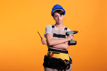 Angry construction worker holding drill gun and screwdriver, posing in studio. Woman dressed as building worker holding renovating tools and power screw drilling gun, serious builder.