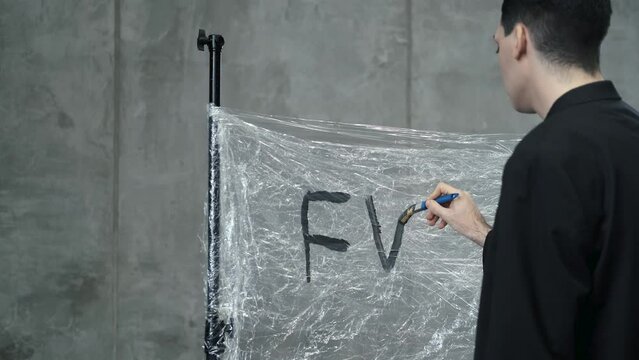 a man writes the letters "FV" on a blackboard with a brush