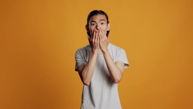 Asian adult sending air kisses on camera, acting funny and romantic in studio. Young carefree person blowing kisses and being flirty, acting sensual with kissy silly face. Natural confidence.
