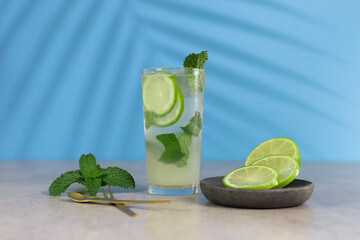 Bright, modern and playful cocktail image of a mojito with green lemon and peppermint with a blue background and a shadow of a palm tree